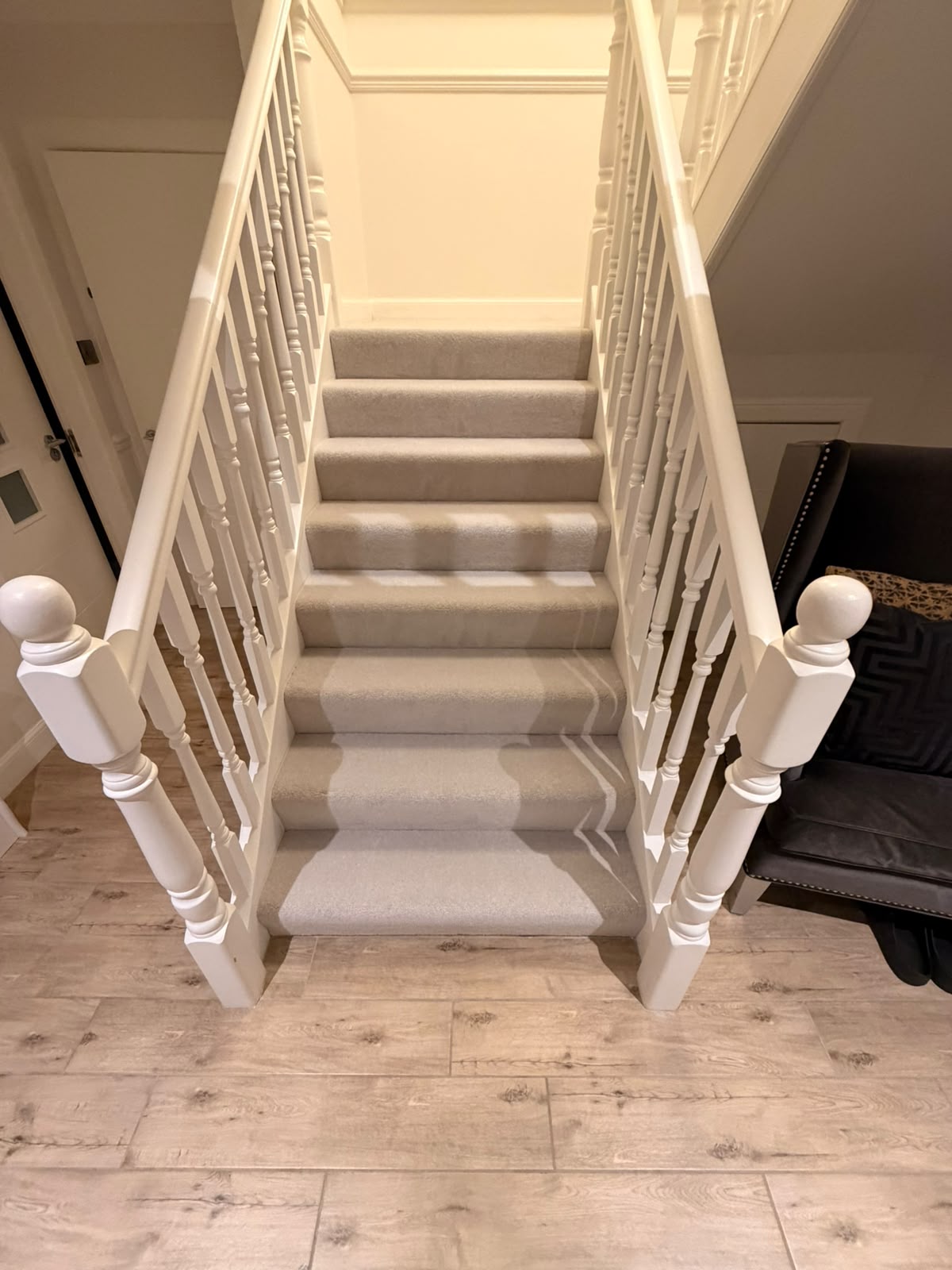Grey carpeted staircase with white spindles above a laminate hallway