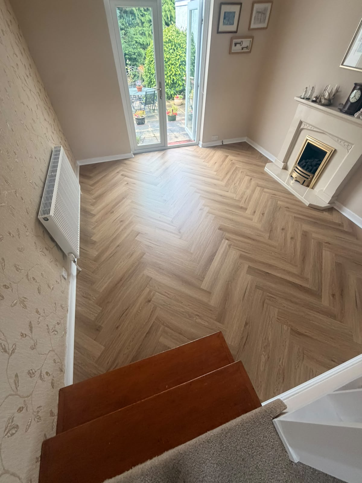 Light-oak herringbone LVT fitted through a lounge, with French doors opening to the garden